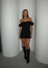 A model wearing a black mini dress with short puffed sleeves and a round neckline, paired with knee-high boots.